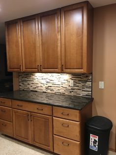 a kitchen with wooden cabinets and black trash can on the counter top in front of it