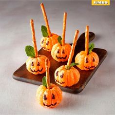 small pumpkins with faces carved into them sitting on a wooden tray next to leaves