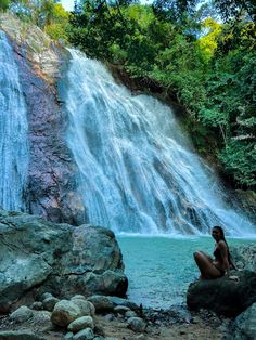 a woman sitting on top of a rock next to a waterfall