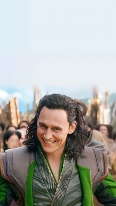 a man with long hair wearing a green vest and smiling at the camera while standing in front of a crowd