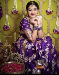 a woman in a purple and gold sari sitting on a chair with her hands clasped to her chin