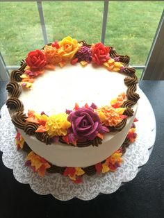 a white cake with flowers on it sitting on a table next to a glass window