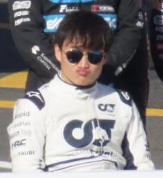 a young man sitting on top of a race car in front of another person wearing sunglasses