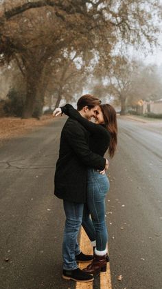 a man and woman standing on the side of an empty road in front of trees