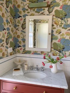 a bathroom with a sink, mirror and flowers on the wall