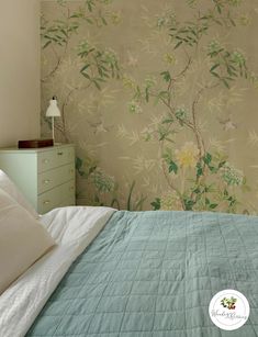 a bed sitting under a window next to a wallpaper covered in green and white flowers