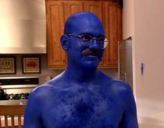 a man with blue paint on his face and chest standing in a kitchen next to a refrigerator