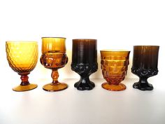 five different colored glass goblets lined up on a white surface with one black and the other yellow