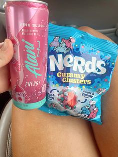 a person holding a candy bar next to a pink and blue drink in a car