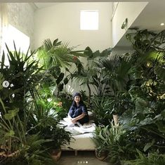 a woman sitting on a bed surrounded by plants