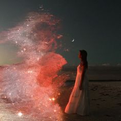 a woman is standing on the beach watching fireworks