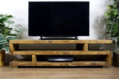 a flat screen tv sitting on top of a wooden stand next to potted plants