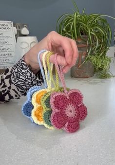 a person is holding some small crocheted bags on a table next to a potted plant