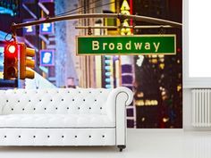 a white couch sitting in front of a wall mounted street sign with the word broadway on it