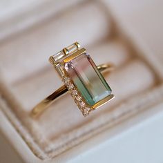 an engagement ring with a green tourmaline surrounded by diamonds in a white box