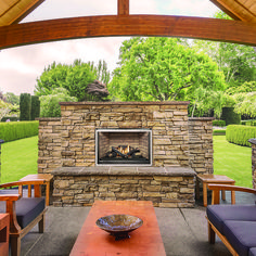 an outdoor fireplace in the middle of a patio with chairs around it and a wooden table