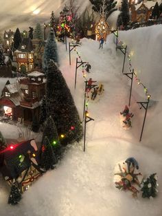 a christmas village with lots of lights and decorations on the trees, snow covered ground