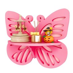 a pink butterfly shaped shelf with candles and other items sitting on it's side