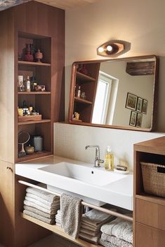 a bathroom sink sitting under a mirror next to a shelf filled with towels and other items