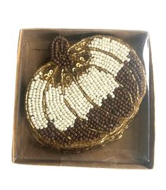 a decorative pumpkin in a box on a white surface with gold trimmings and beads