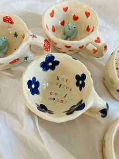 four ceramic bowls with designs on them sitting on a white tableclothed surface, one has two little birds in the bowl