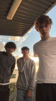 three young men standing next to each other in front of a building under a blue sky