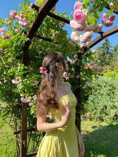 a woman in a yellow dress standing under a trellis with pink flowers on it