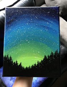 someone is holding up a small painting with the aurora bore in the sky above them