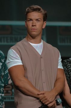 a man with his arms crossed standing in front of a microphone and wearing a vest