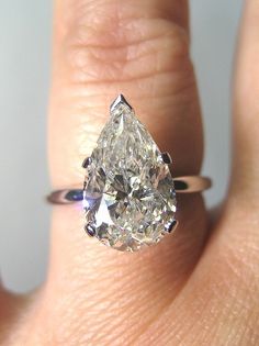 a woman's engagement ring with a pear shaped diamond in the center, on her finger