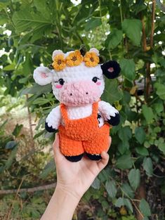 a hand holding a small stuffed cow wearing an orange and white outfit with flowers on it's head