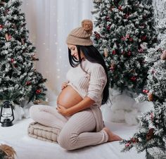 a pregnant woman sitting in front of christmas trees with her belly wrapped up and wearing tight pants