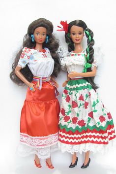 two dolls are standing next to each other on a white surface, one is wearing a red and green dress