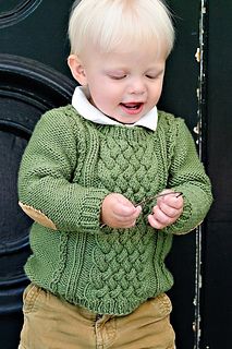 a little boy standing in front of a black door wearing a green sweater and khaki pants