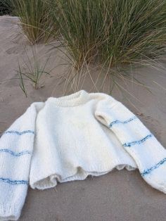 a white sweater laying on top of a sandy beach next to tall grass and sea oats