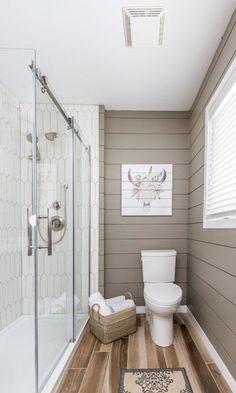 a white toilet sitting in a bathroom next to a walk in shower and wooden floors