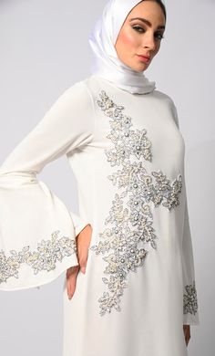 Step into the grace and charm of Eid celebrations with our exclusive Abaya Collection, featuring the epitome of elegance and sophistication. Our machine embroidered Abaya, meticulously adorned with pearl and stone handwork, is a testament to timeless beauty and exquisite craftsmanship. Crafted with meticulous attention to detail, this Abaya boasts delicate machine and Hand embroidery with stones and Pearls that adorns every inch, creating a mesmerizing tapestry of intricate patterns. Each stitch reflects a dedication to perfection, enhancing the allure of this traditional garment. The Abaya also features Round neck, flared sleeves , back zip closure and a loose belt for a cinched waist silhouette effect. Size & FitModel height is 5’9’ and is wearing a Small sizeMaterial & CareMaterial: Pan Luxury White Abaya With Dabka Details, White Abaya With Modesty Panel For Eid, Modest Wedding Hijab For Eid, Festive White Floor-length Abaya, Elegant Long Sleeve Dresses For Eid, Elegant White Long Sleeve Abaya, Elegant Bell Sleeve Wedding Dress, Elegant Long Abaya For Festive Occasions, Festive White Embellished Abaya