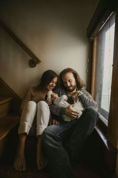 a man and woman are sitting on the stairs with their baby in their arms as they hold each other