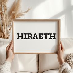 a person holding up a framed sign that says hirafeth on it in front of a white couch