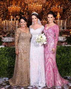 three women standing next to each other in front of a chandelier filled with candles