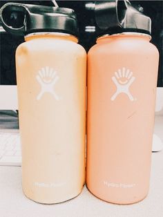 two hydro flasks sitting next to each other on a desk with a computer in the background