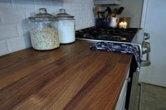 a wooden counter top in a kitchen next to a stove and cabinets with glass jars on it