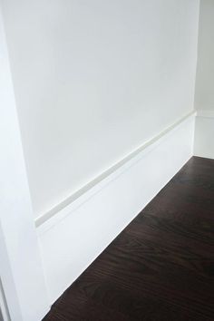 the corner of a room with white walls and wood flooring is shown in this image