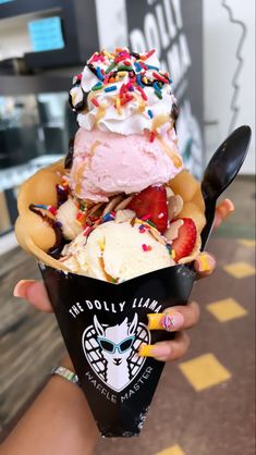 a person holding an ice cream sundae with sprinkles and strawberries