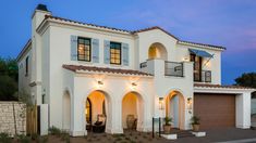 a large white house with lots of windows and lights on it's front porch