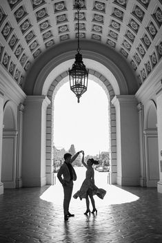 two people are dancing in an archway with a light fixture hanging from the ceiling above them