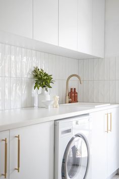 a washer and dryer in a white kitchen with gold handles on the counter