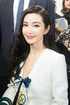 a woman with long hair wearing a white dress and smiling at the camera while standing next to other people