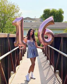 a woman standing on a bridge holding two large balloons in the shape of the number 20