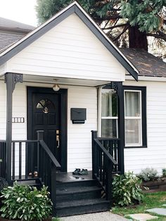 a small white house with black front door and steps leading up to the entryway